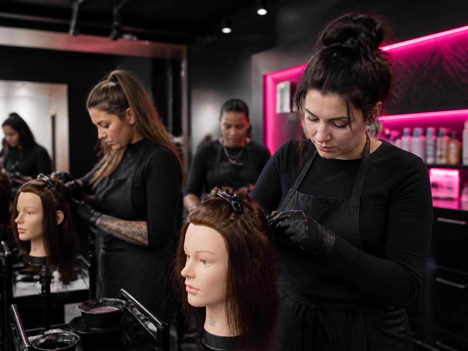 Adult cosmetology students practicing color technique at stations in a training lab